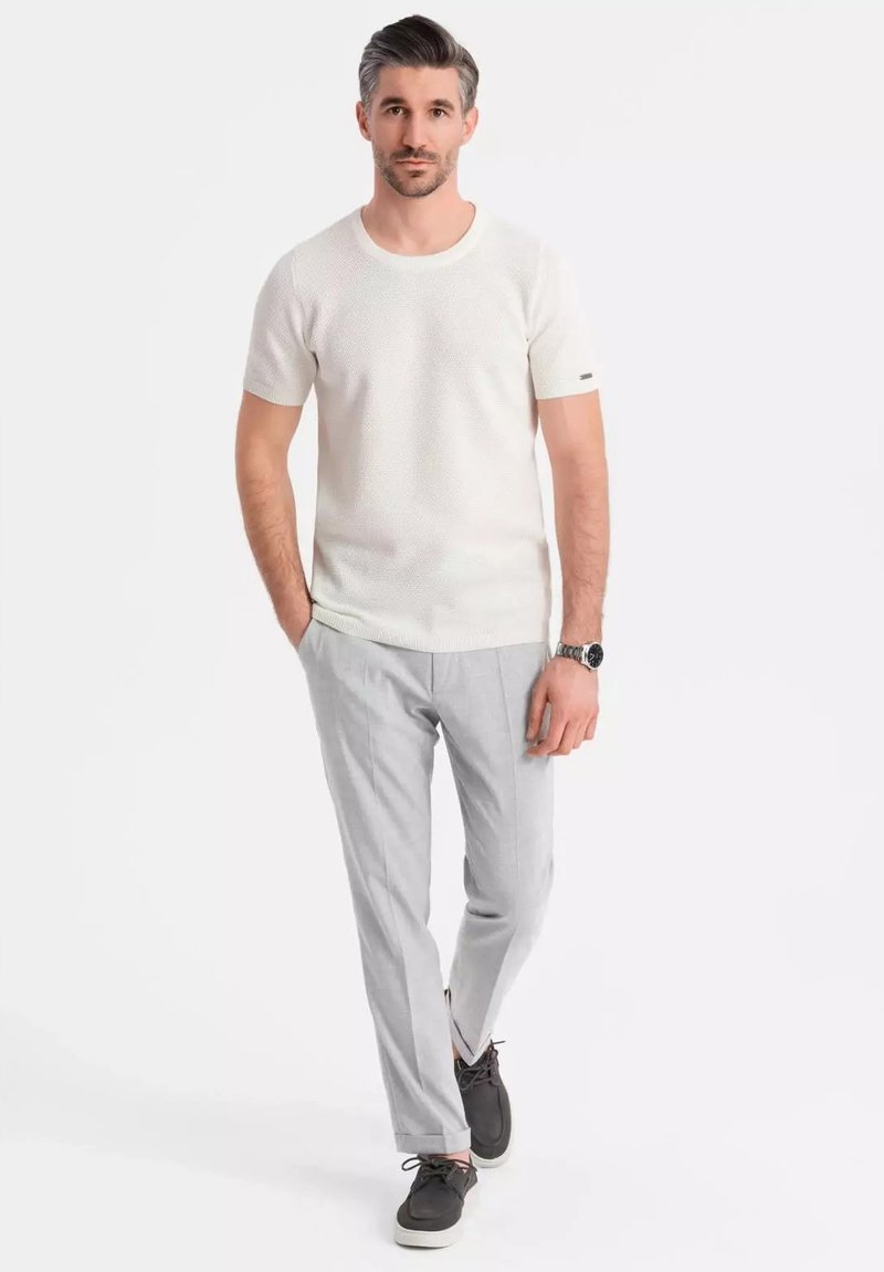 Camisa de punto blanca de manga corta con cuello redondo, acompañada de pantalones ajustados gris claro y zapatos oscuros con diseño de cordones.