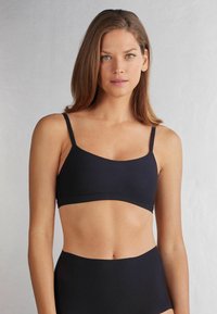Svart, sömlös bralette med tunna justerbara remmar och en mjuk, slät textur, med en enkel, modern design.