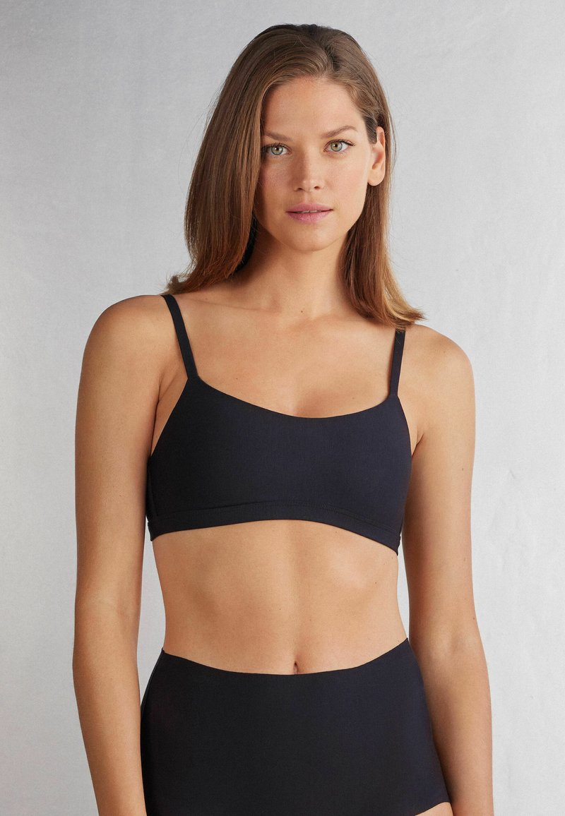 Svart, sömlös bralette med tunna justerbara remmar och en mjuk, slät textur, med en enkel, modern design.