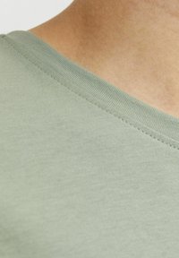 Camiseta verde claro con diseño de cuello en V, textura suave y costuras estrechas a lo largo del cuello. Vista en primer plano de la tela.