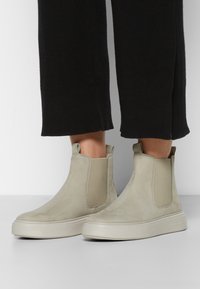 Beige Wildleder Chelsea-Stiefel mit elastischen seitlichen Einsätzen und einer strukturierten Gummisohle, die ein niedriges Profil für vielseitigen Tragekomfort aufweisen.