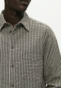 Lightweight button-up shirt in brown and white vertical stripes. Features a classic collar, chest pocket, and textured fabric.