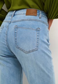 Jeans de mezclilla azul claro con un diseño ajustado, que cuentan con una etiqueta de cuero marcada con "DENIM" y costuras contrastantes en los bolsillos traseros.