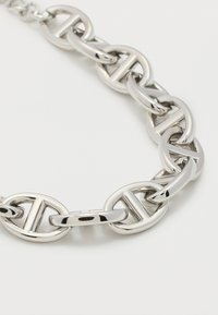 Κοντινό πλάνο λαμπερών αλυσίδων από ασημένια κρίκους με οβάλ σχήματα και οριζόντιες μπαρες σε απλό λευκό φόντο.