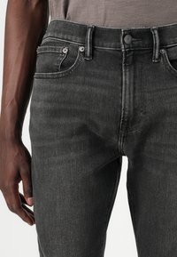 Vaqueros de mezclilla gris oscuro con un diseño ajustado, que cuentan con una cintura de altura media, cinco bolsillos y una textura sutilmente desgastada. Detalles en metal.