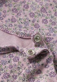 Tkanina w kwiatowy wzór w jasnoróżowym kolorze z fioletowymi i zielonymi akcentami. Posiada srebrne zatrzaski oraz teksturowane wykończenie na brzegach.