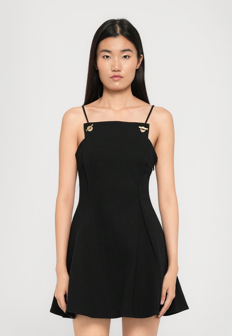 Robe sans manches noire avec un bustier structuré, une jupe évasée et des accents dorés sur les bretelles. Tissu lisse et design minimaliste.