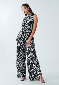 Mustvalge sebratriibuline varrukateta top ja laia säärega püksid, millel kõrge kaelus ja külje lõhikud. Sile kangapind.