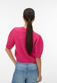 Pull en maille rose avec manches courtes bouffantes ; texture douce et duveteuse. Associé à un jean taille haute bleu clair.