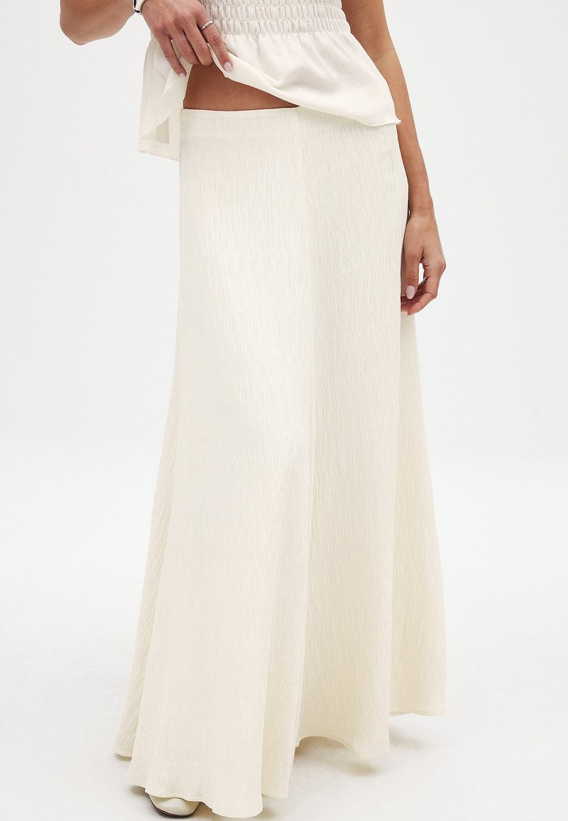 Kermainen, pitkä maksihame, jossa on tekstuuripinta. Hameessa on istuva vyötärö ja valuva siluetti, joka on yhdistetty löysään, eloisaan toppiin.