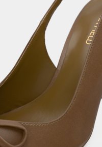 Κοντινό πλάνο καφέ σουέτ ψηλοτάκουνων παπουτσιών με ανοιχτές μύτες και λείο εσωτερικό επένδυση σε λευκό φόντο.