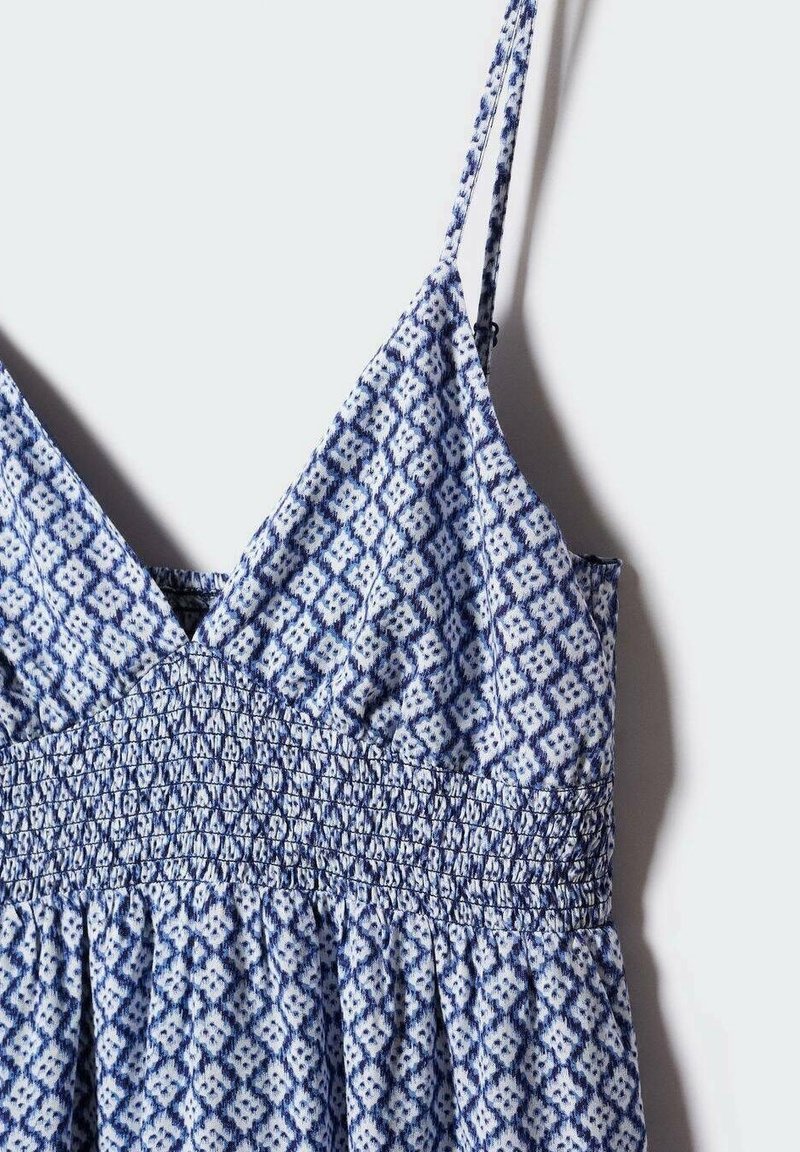 Robe sans manches à motif bleu et blanc avec fines bretelles et taille smockée, présentée suspendue sur un fond clair.