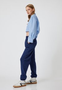 Geknipt blauw gestreept shirt, marineblauwe sweatpants met een elastische tailleband en witte sneakers met zwarte accenten. Soepele texturen, relaxte pasvorm.