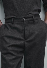 Pantalons en mélange de laine gris avec une texture lisse, coupe ajustée, poches latérales et fermeture à un bouton à la taille.