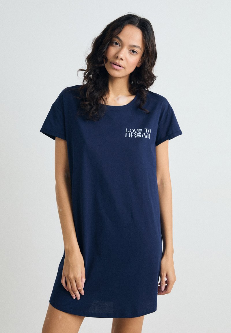 Mörkblå bomulls-t-shirtklänning med korta ärmar, rundad halsringning och texten "LOVE TO DREAM" i vitt på vänster bröst. Slät textur.