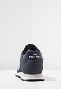 Zapatilla navy con parte superior de cuero suave, forro de malla, logo blanco en el talón, acentos grises y suela de goma negra texturizada.