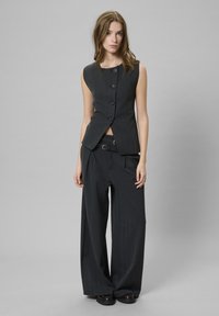 Vesta în dungi, de culoare gri închis, cu un design ajustat și cinci butoane, asortată cu pantaloni largi și cu talie înaltă. Textură a țesăturii netedă.