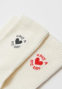 Calzini bianchi a coste con un cuore nero e la scritta "HAVE A" su un calzino, e un cuore rosso con la scritta "HAVE A" sull'altro.