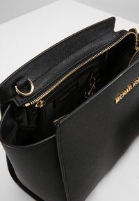 Černá kožená kabelka s texturovaným povrchem, zapínáním na zip a kováním ve zlaté barvě. Interiér obsahuje kapsy a značkovou štítek.