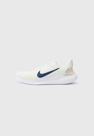 Baskets de course Nike blanches avec un tissu texturé, logo swoosh bleu marine et accents crème au niveau du talon. Présente un design léger et flexible.
