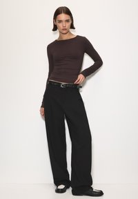 Brązowy, dopasowany top z długim rękawem w połączeniu z luźnymi czarnymi spodniami. Stylizacja zawiera czarny pas oraz czarne buty z białymi akcentami.