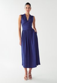 Mornarička plava haljina bez rukava s V-izrezom, priljubljenim korzetom i nabrano strukom, koja prelazi u suknju punog dužine, s bočnim džepovima.