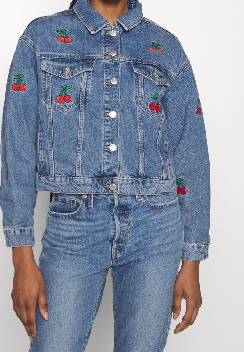 Denim jakki med en kortet design, med rød kirsebærbroderi og sølvknapper. Blått stoff med klassisk krage og brystlommer.