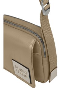 Beige crossbody taske med en struktureret overflade, featuring en sølvfarvet lynlås og et logo-patch. Justerbar strop med brandingdetalje.
