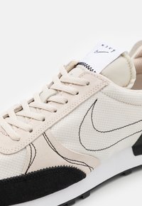 Lichtbeige sneakers met zwarte accenten, voorzien van een bovenwerk van gestructureerde stof, contrasterende stiksels en een gepolsterde tong met logo-label.