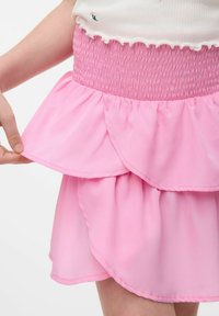 Falda rosa en capas con una cintura fruncida, hecha de tela ligera. La capa inferior presenta un diseño fluido y con volantes.