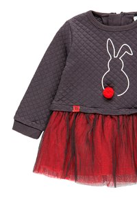Ciemnoszara, pikowana bluzka z motywem królika, z detalem w postaci czerwonego pom-pomu, warstwowa spódnica z czerwonego tiulu oraz mała czerwona metka z logo na końcu.