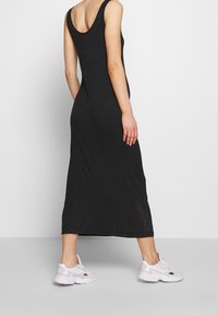 Czarna, bezrękawnikowa sukienka midi z okrągłym dekoltem i dopasowanym krojem, w połączeniu z białymi sportowymi sneakersami. Gładka faktura materiału.