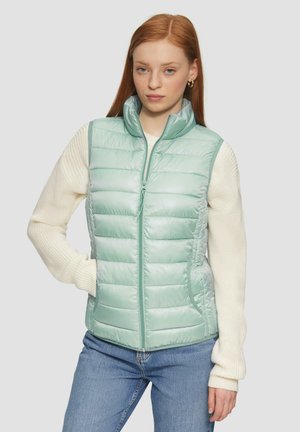 Light green padded vest with a high collar, front zipper, and two side pockets. Features a smooth texture and quilted design. Paired with a cream sweater.