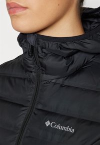 Zwarte gewatteerde jas met ritssluiting op de kraag, voorzien van een quilted ontwerp en het Columbia-logo in het grijs op de linkerkant van de borst. Soepele stofstructuur.
