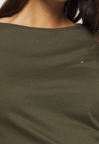 Top in cotone leggero color verde oliva con scollatura ampia e maniche corte. Presenta un piccolo logo del brand sul davanti.