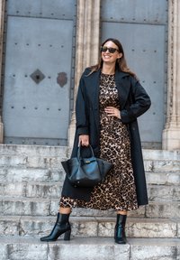 Black trench coat over a leopard print dress, black ankle boots, and a black handbag. Smooth textures with a mix of patterns and solid colors.