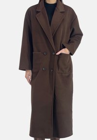 Brun trenchcoat i ullblandning med dubbelknäppt front, spetsiga slag och två sidfickor. Mjuk textur, midjelång design.