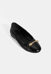 Schwarze Lederflats mit abgerundeter Zehenpartie, die auf der Vorderseite mit einer goldfarbenen Schnalle verziert sind und eine glatte, glänzende Oberfläche haben.
