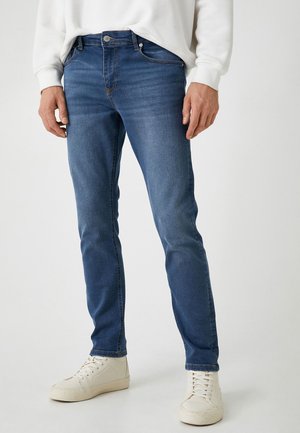 Vaqueros de denim azul con corte slim, que cuentan con cinco bolsillos, cremallera y costuras sutiles. Combinados con zapatillas deportivas blancas de caña alta.