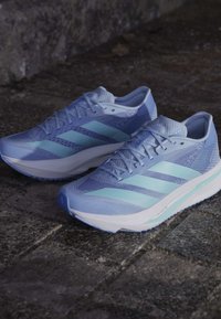Hellblaue Sportschuhe mit einem strukturierten Mesh-Obermaterial, drei dunkelblauen Streifen, einer weißen Zwischensohle und einer gemusterten Laufsohle.