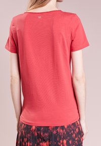 T-shirt rossa a maniche corte con un design aderente, texture liscia e un piccolo logo sulla parte posteriore del collo.