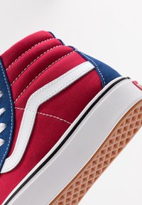 Gros plan du talon d’une basket rouge, bleue et blanche avec une bande latérale blanche, une semelle intermédiaire blanche et une semelle extérieure en gomme à motif gaufré.