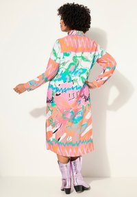 Robe longue à manches longues colorée avec des motifs abstraits en rose, vert et bleu. Dotée d'un col et d'un ourlet enveloppant contrasté. Portée avec des bottes métalliques roses.