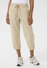 Pantalon court beige clair à fines rayures verticales, taille élastique avec cordon de serrage, poches latérales et poignets froncés.