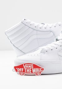 Vita högskor i läder med texturerad design, rund tå och en röd "Vans Off The Wall"-etikett vid basen.