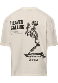 Cremfarbene Baumwoll-T-Shirt mit einem schwarzen Skelettgrafik in kniender Position und dem Text "HEAVEN CALLING" sowie "DROPSIZE".