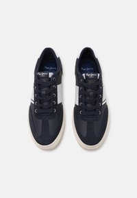 Tengerészekkel díszített, fehér részletekkel ellátott, sima és velúr textúrák kombinációjával készült sötétkék sneakers, kerek orral, fűzős zárással és kontrasztos gumi talppal.