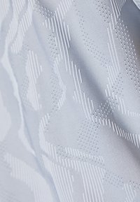 Tejido de color azul claro con un patrón abstracto texturizado que presenta elementos blancos en relieve y franjas horizontales, exhibiendo un acabado liso.