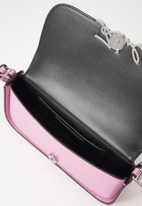 Kompakte Handtasche mit einem pinken Lacklederboden und schwarzem Innenraum. Enthält ein silbernes Logo-Detail und einen sicheren Druckverschluss.