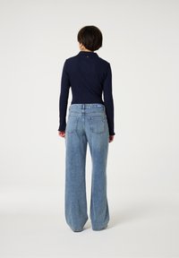 Marineblauwe ribgebreide longsleeve top gecombineerd met lichtblauwe wijde jeans. De jeans hebben achterzakken en een label op de tailleband.